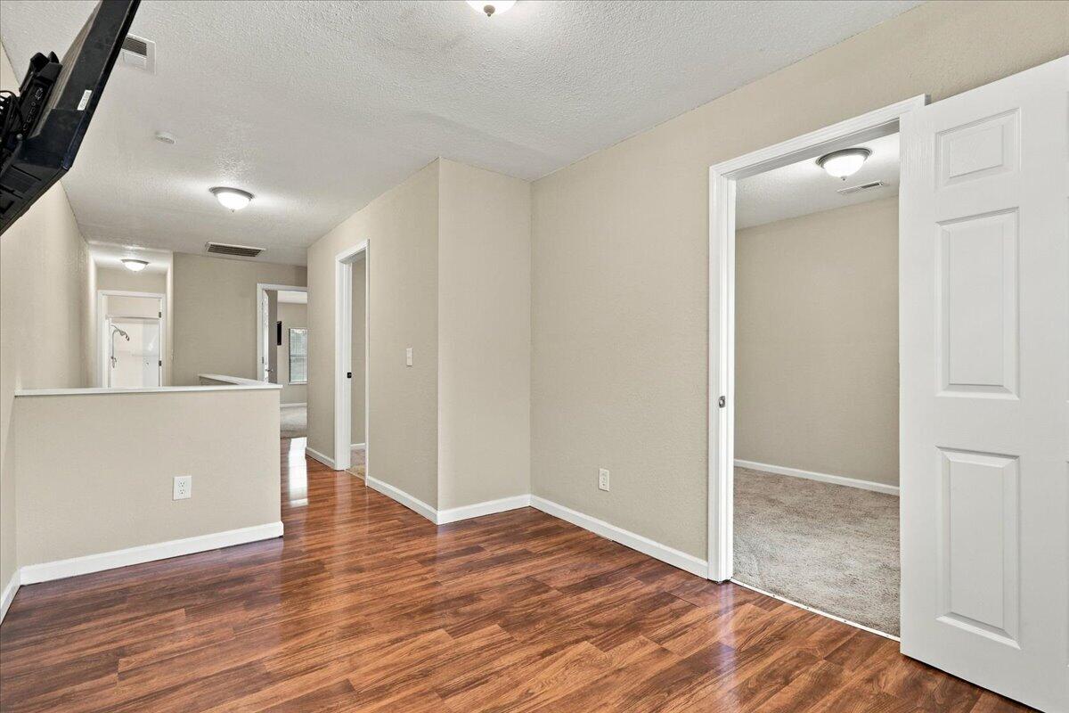 Vacant interior with wood-look floors and an open doorway to a carpeted room.