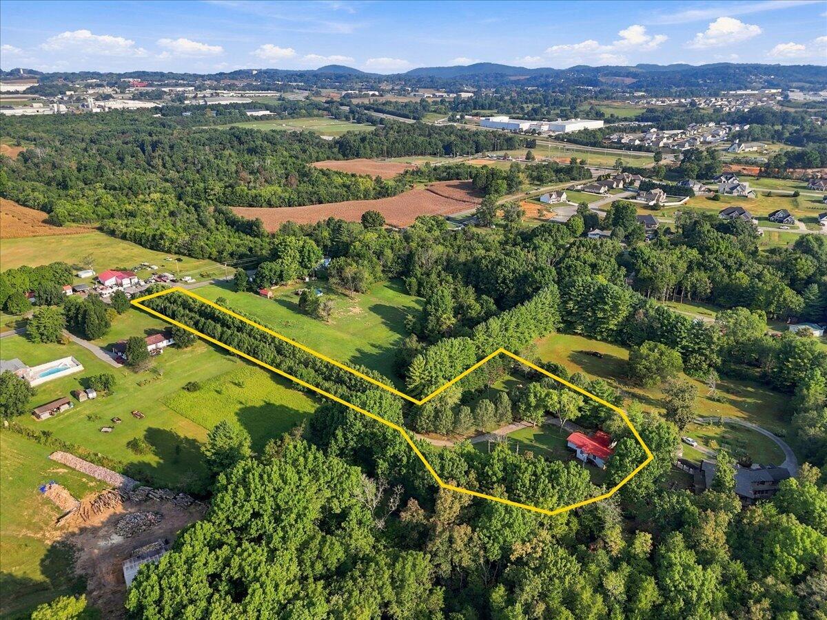 Aerial view of a wooded property outlined in yellow, with open grass and a red-roofed house.