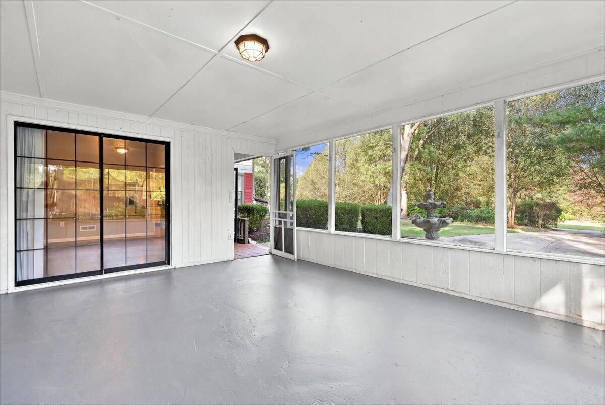 Enclosed sunroom with large windows overlooking a landscaped yard and tiered fountain.