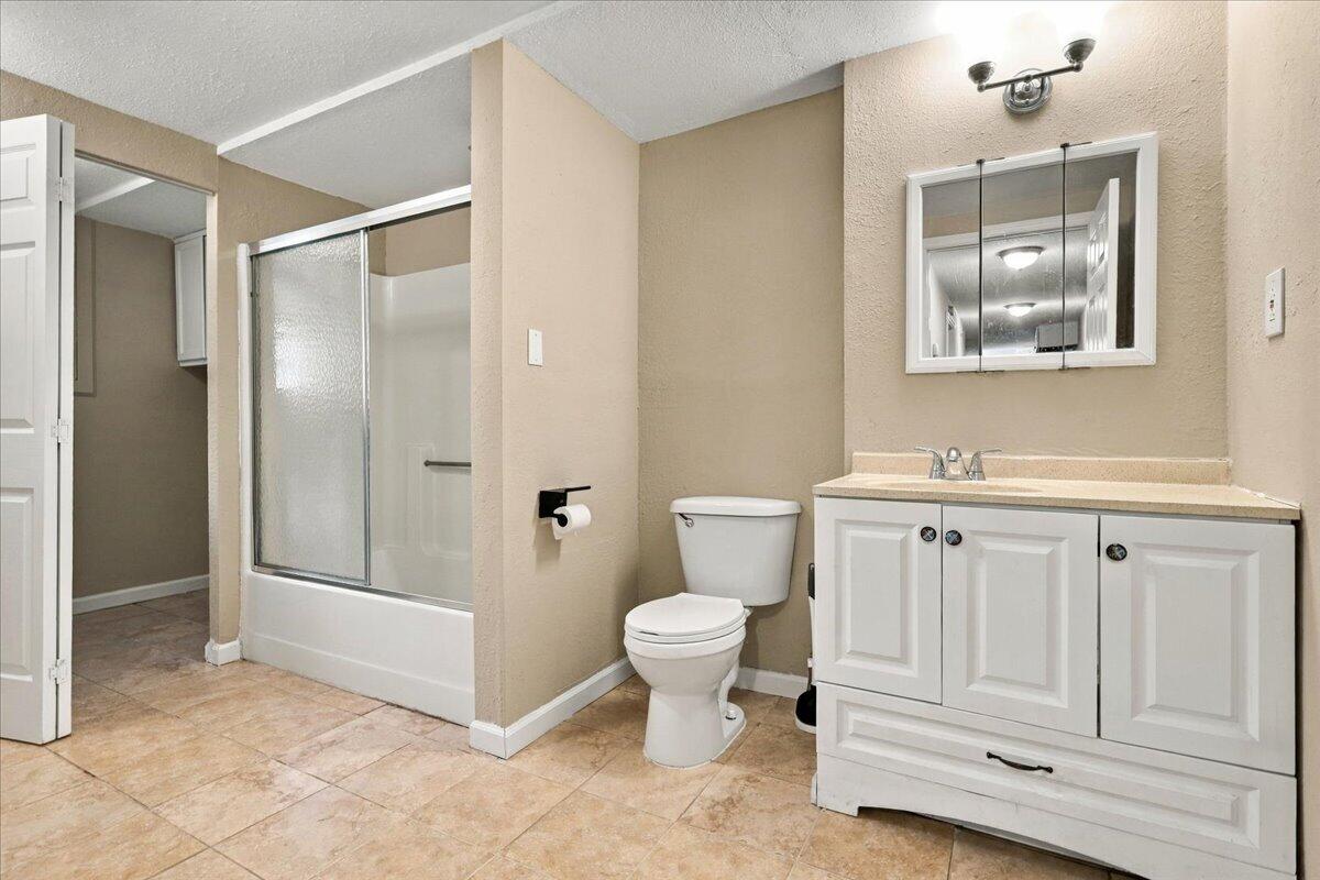 Bathroom with a glass-enclosed tub and shower beside a white vanity and toilet.
