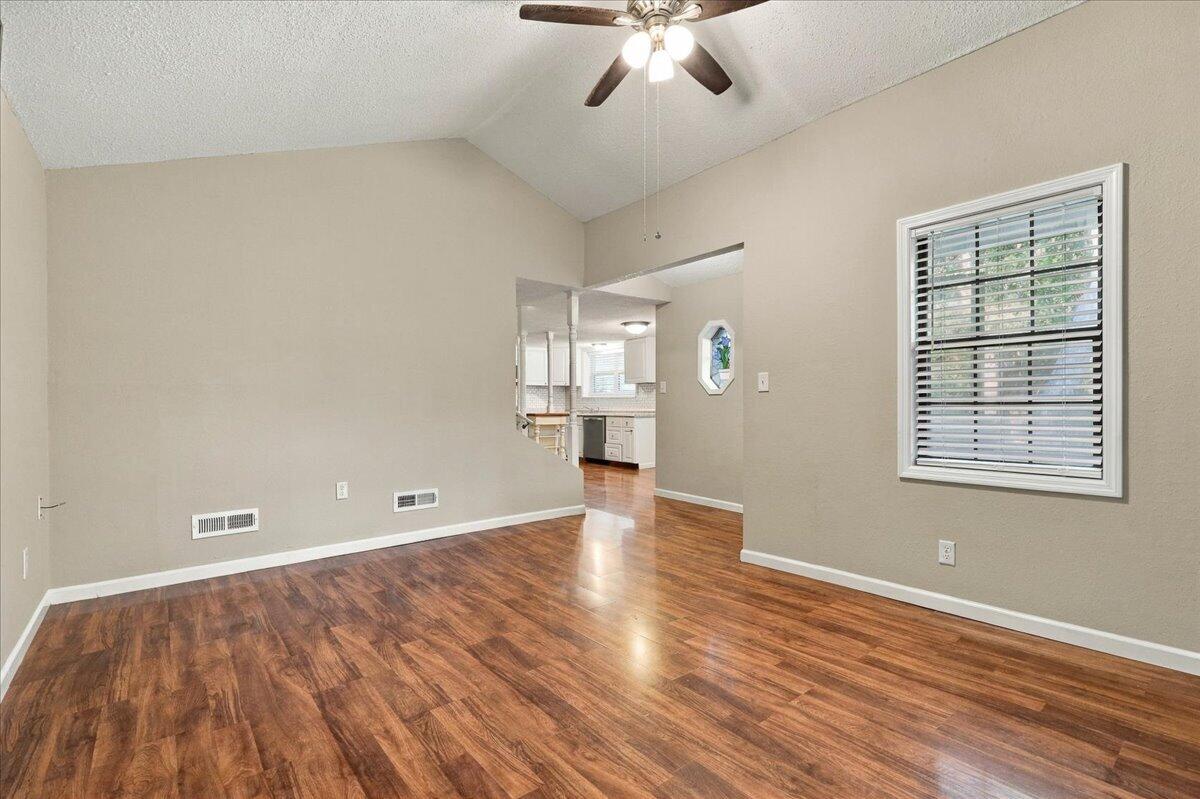 Empty living room with wood-look flooring, a vaulted ceiling, and an opening to the kitchen.