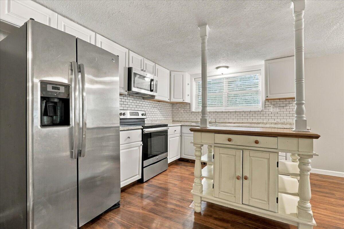 Kitchen with white cabinets, stainless steel appliances, subway tile backsplash, and a wood-topped island.