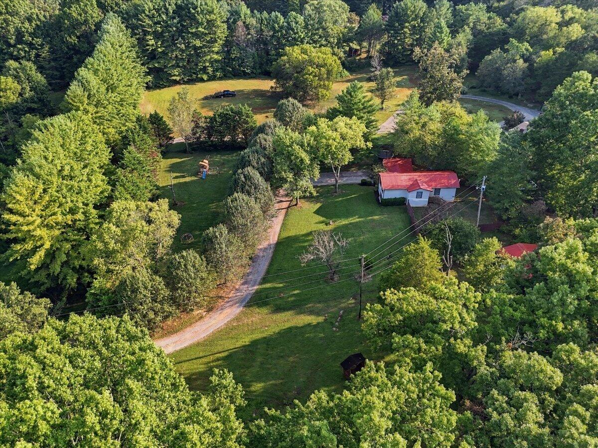 Aerial view of a red-roofed house amid wooded grounds and broad lawns, with a winding gravel driveway.