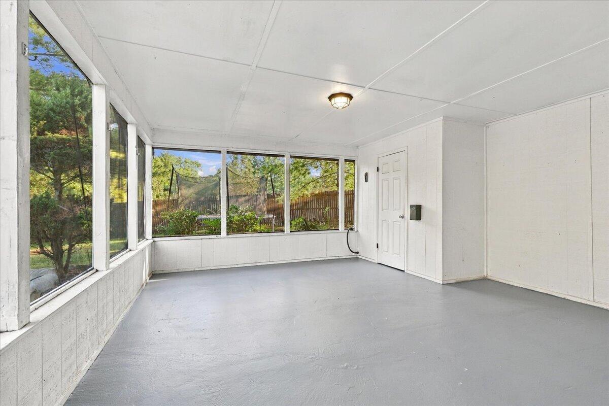 Enclosed sunroom with large windows overlooking trees and a fenced yard.
