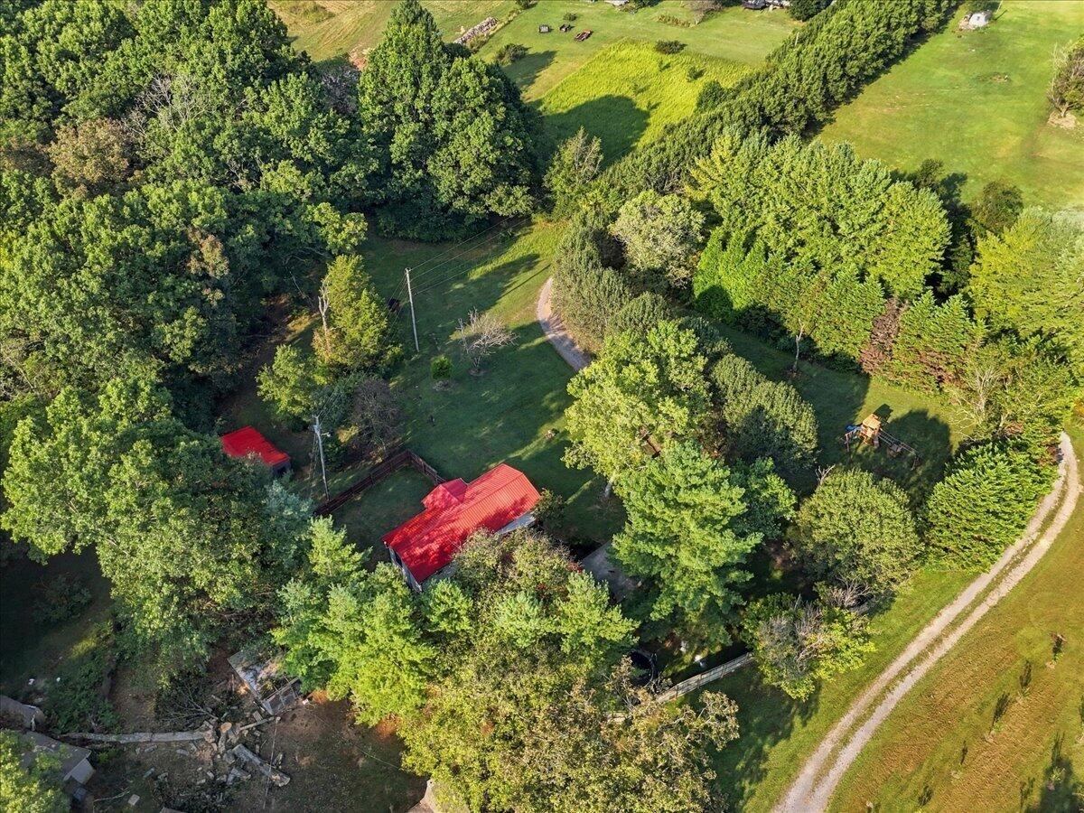 Aerial view of a wooded property with a grassy clearing, red-roofed building, and gravel drive.