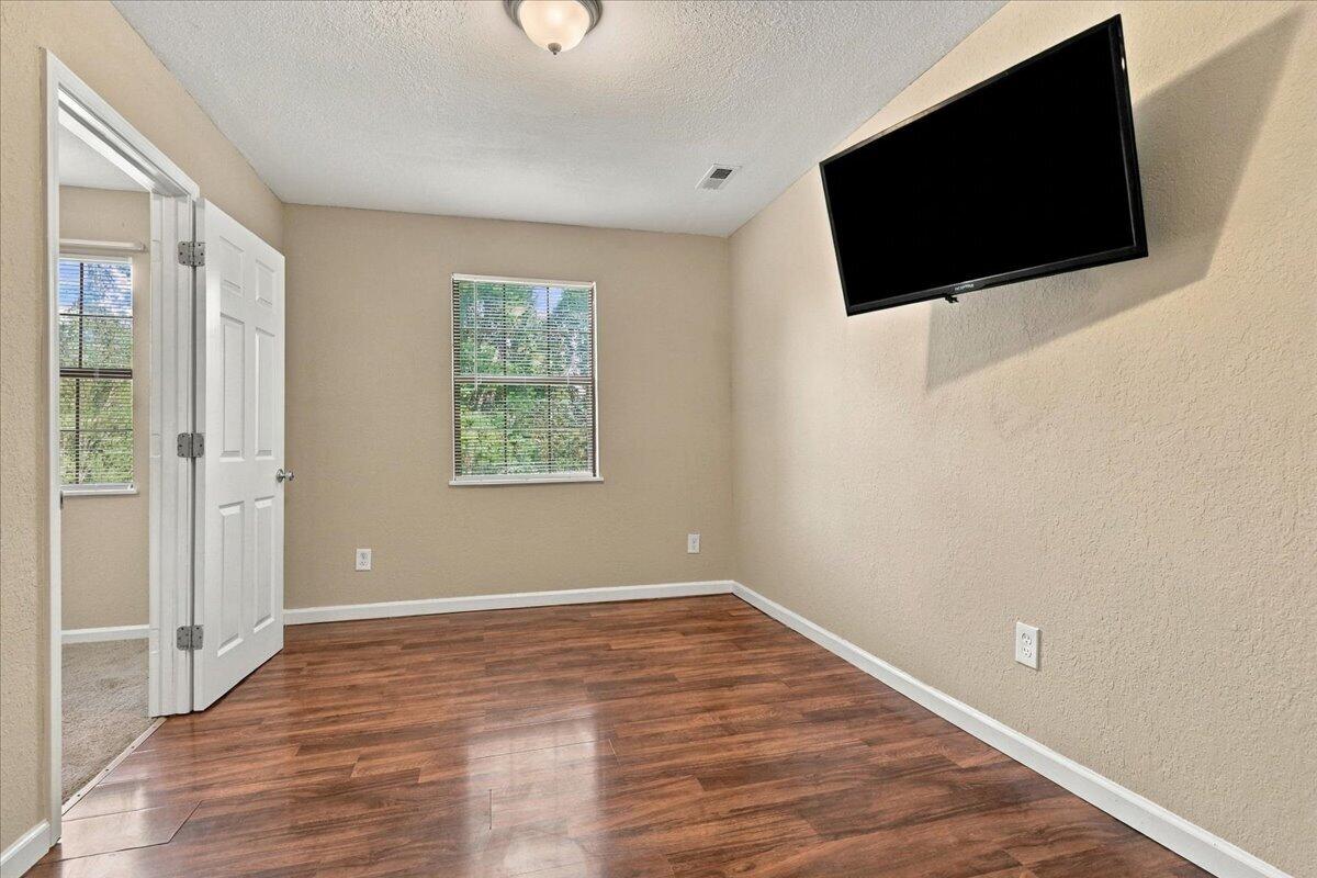 Unfurnished room with wood-look flooring, a window with blinds, and a wall-mounted television.
