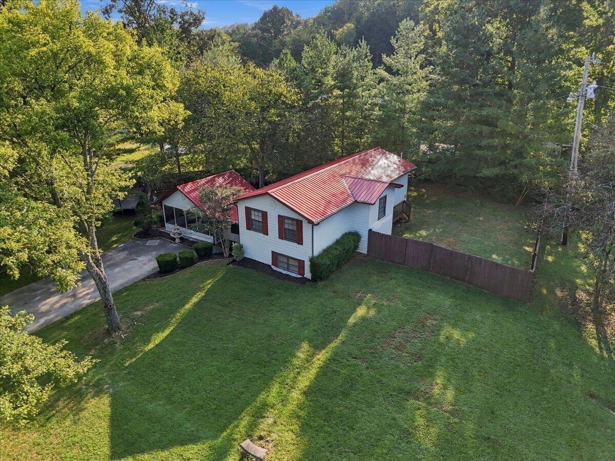 Aerial view of a white house with a red metal roof, surrounded by a lawn and mature trees.