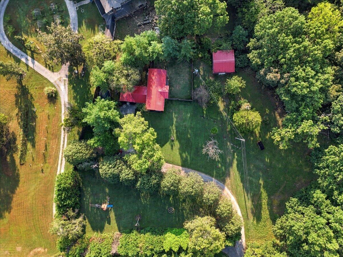 Aerial view of a red-roofed home, broad lawn, curved driveway, and tree-lined grounds.