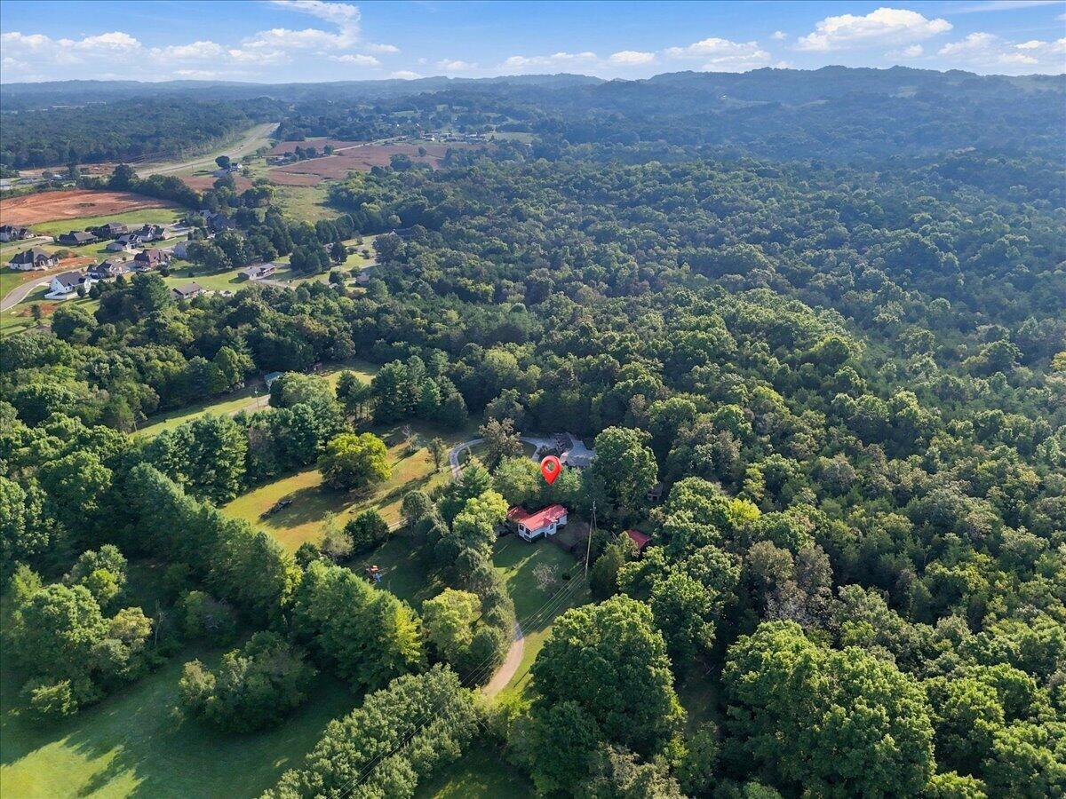 Aerial view of a wooded property with a home, open lawn, and distant ridgelines.