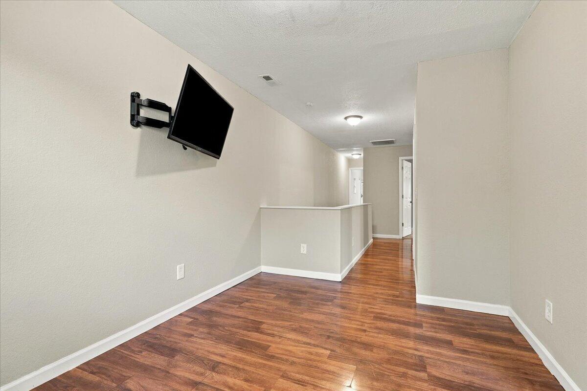 Empty hallway with reddish-brown plank flooring, a wall-mounted TV, and a short half-wall counter.