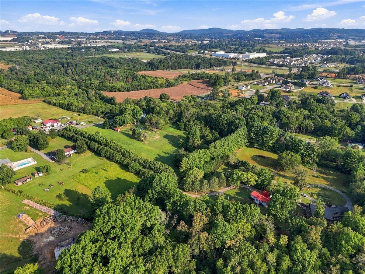 Aerial view of wooded acreage and open fields, with nearby homes and rolling hills in the distance.