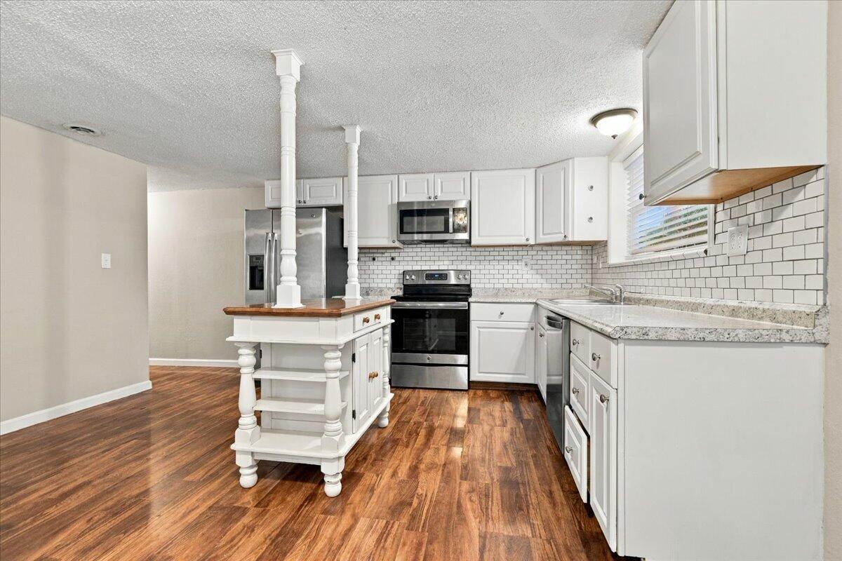 Kitchen with white cabinets, stainless steel appliances, subway-tile backsplash, and a wood-topped island.