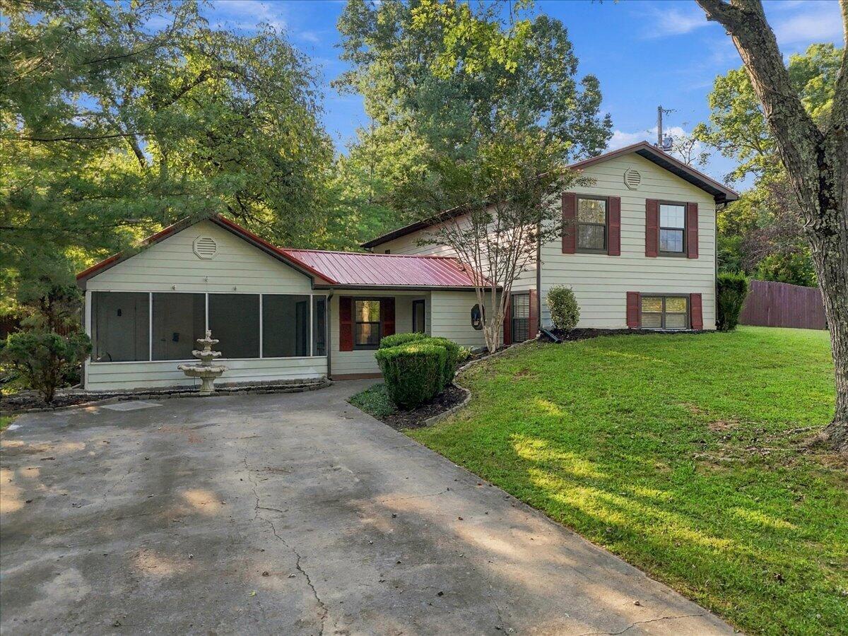 Two-story house with a red metal roof, screened porch, and tree-shaded driveway.