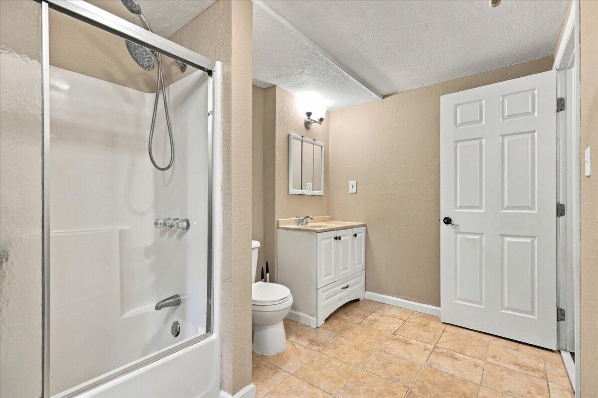 Bathroom with a white tub and shower, vanity, and tan tile floor.