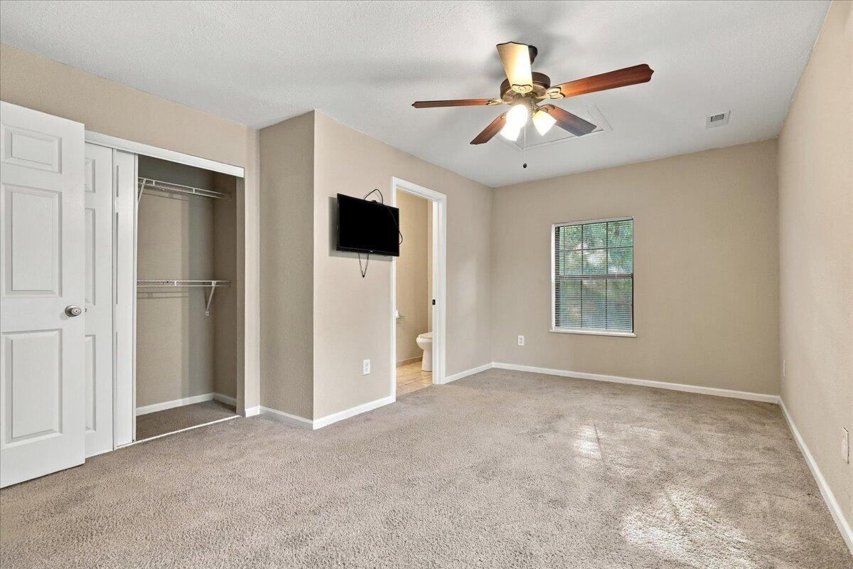 Unfurnished bedroom with beige carpet, an open closet, ceiling fan, and bathroom doorway.