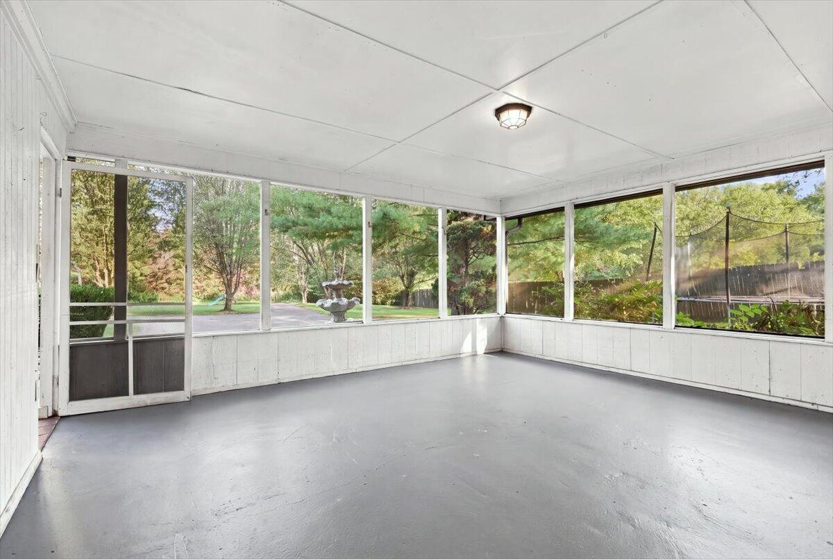 Empty sunroom with large windows overlooking a leafy yard and fountain.