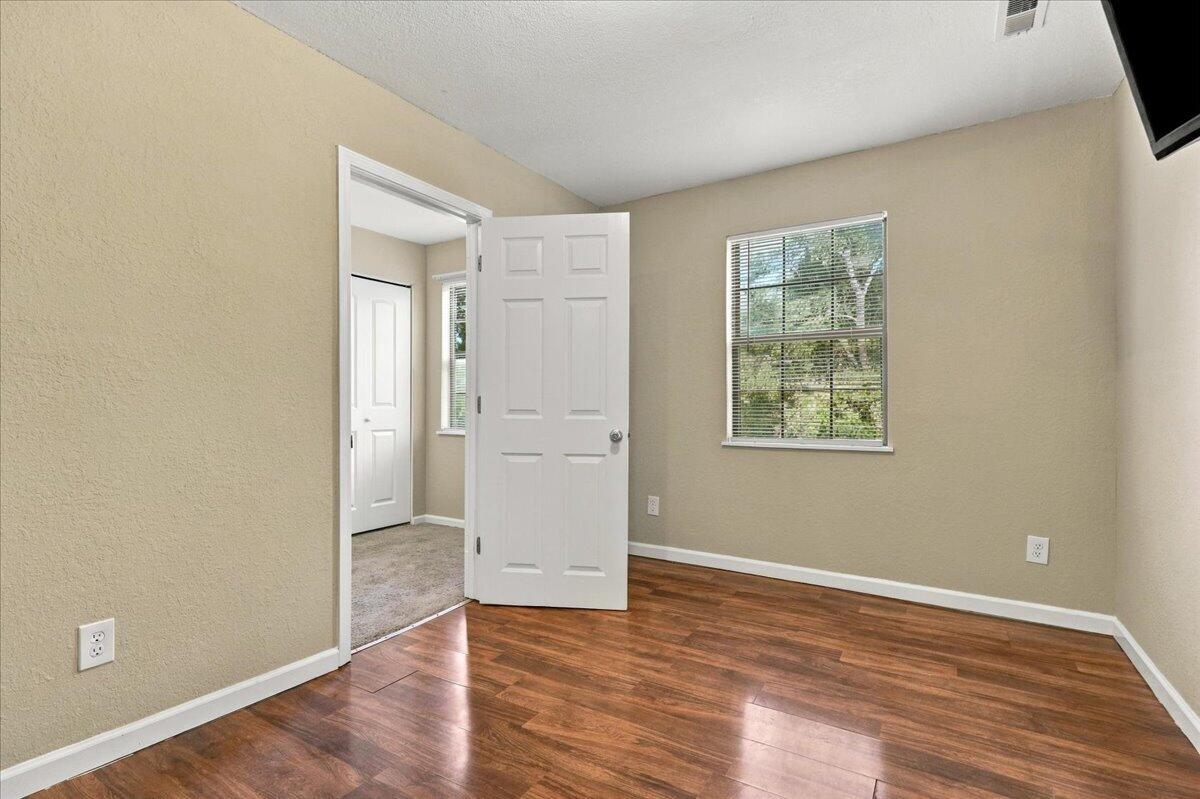 Vacant bedroom with hardwood floors, beige walls, and an open door to a carpeted room.