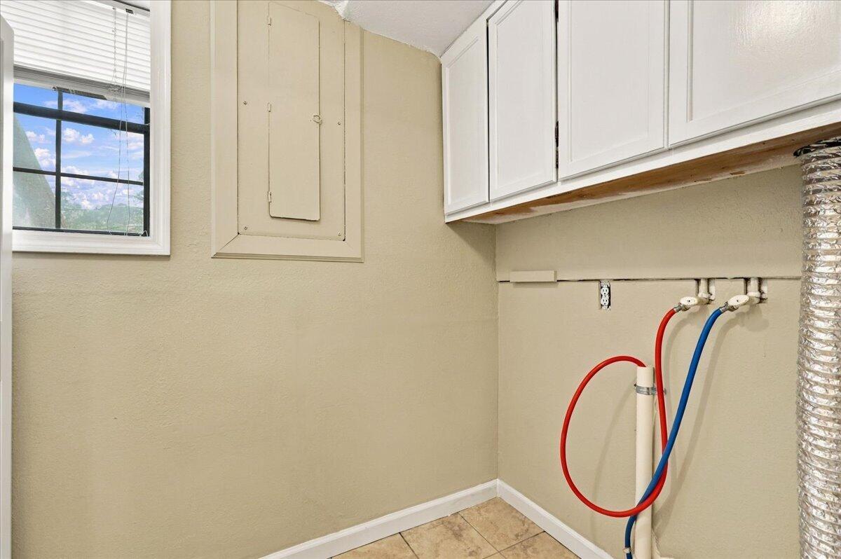 Laundry room with washer hookups, white cabinets, and a window with blinds.
