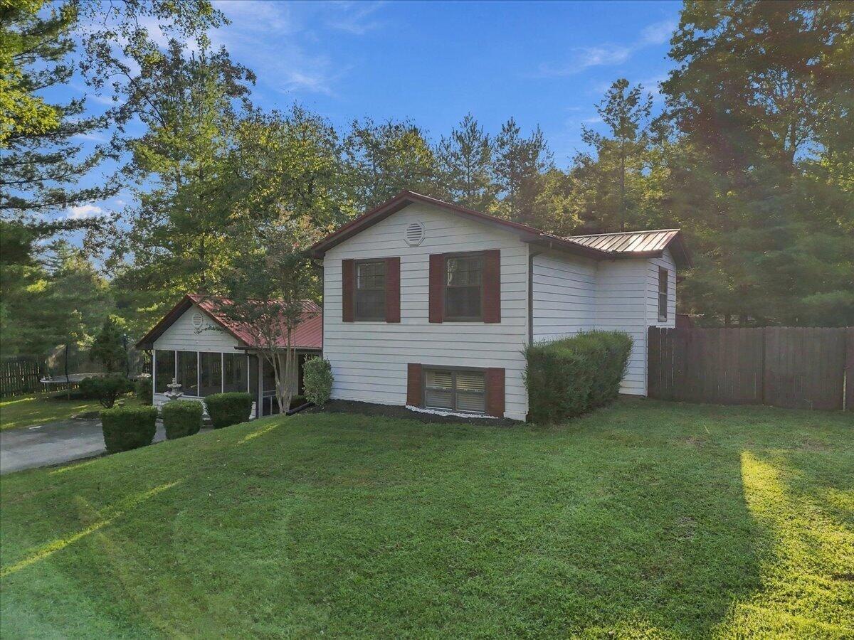 White two-story house with red trim, a screened porch, and a sloping lawn.