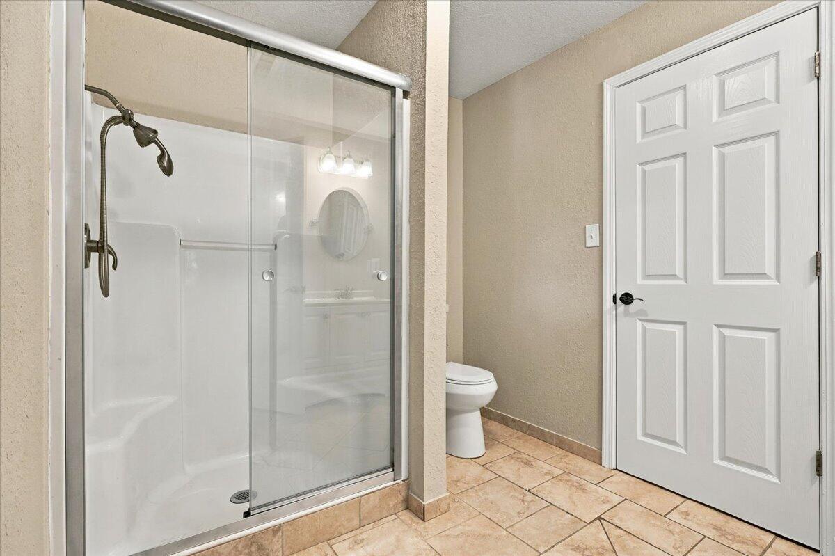 Bathroom with a glass shower, dark fixtures, toilet, and tan tile floor.