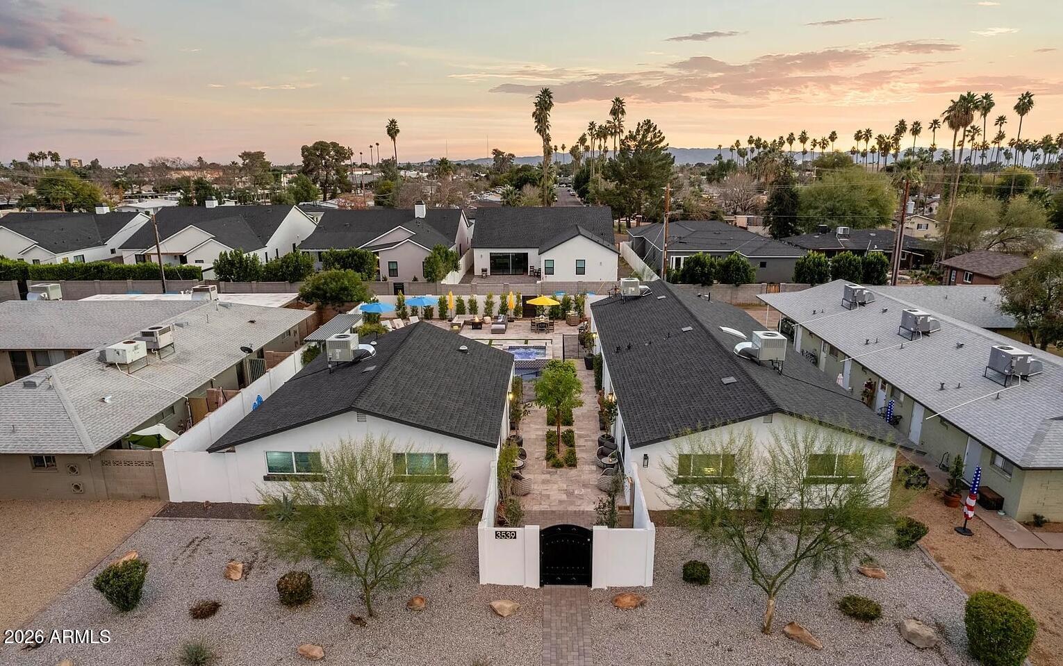 Aerial view of a gated home with a landscaped courtyard and pool, surrounded by neighboring homes and palm trees.