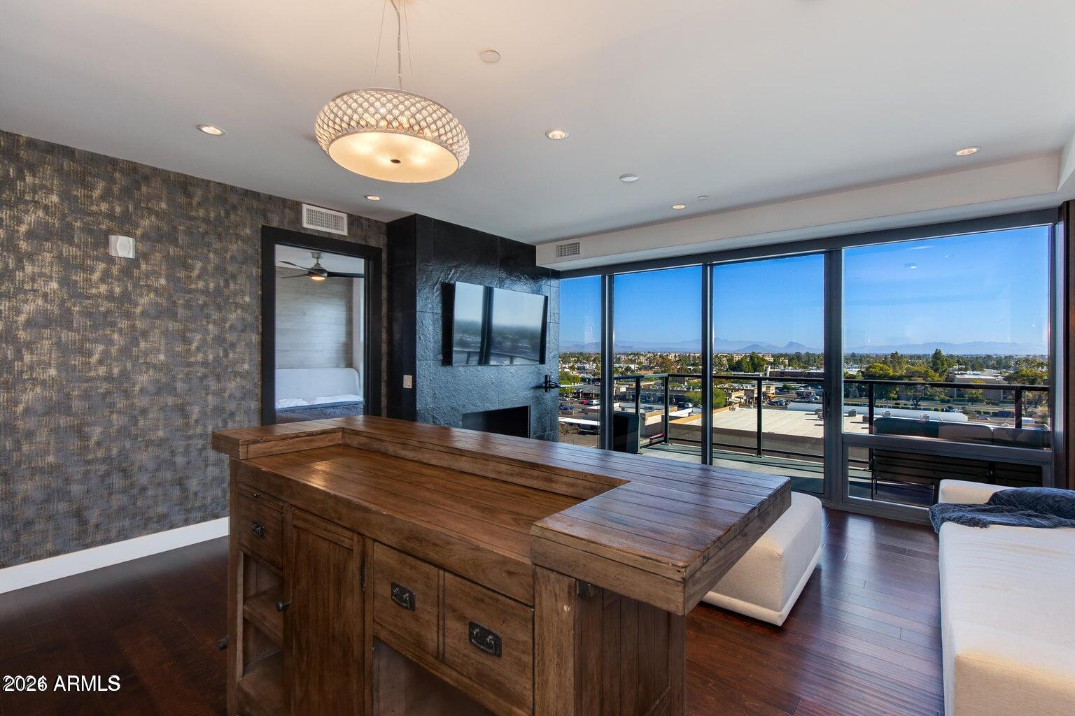 Modern condo living area with a wooden desk and floor-to-ceiling windows overlooking the city and mountains.