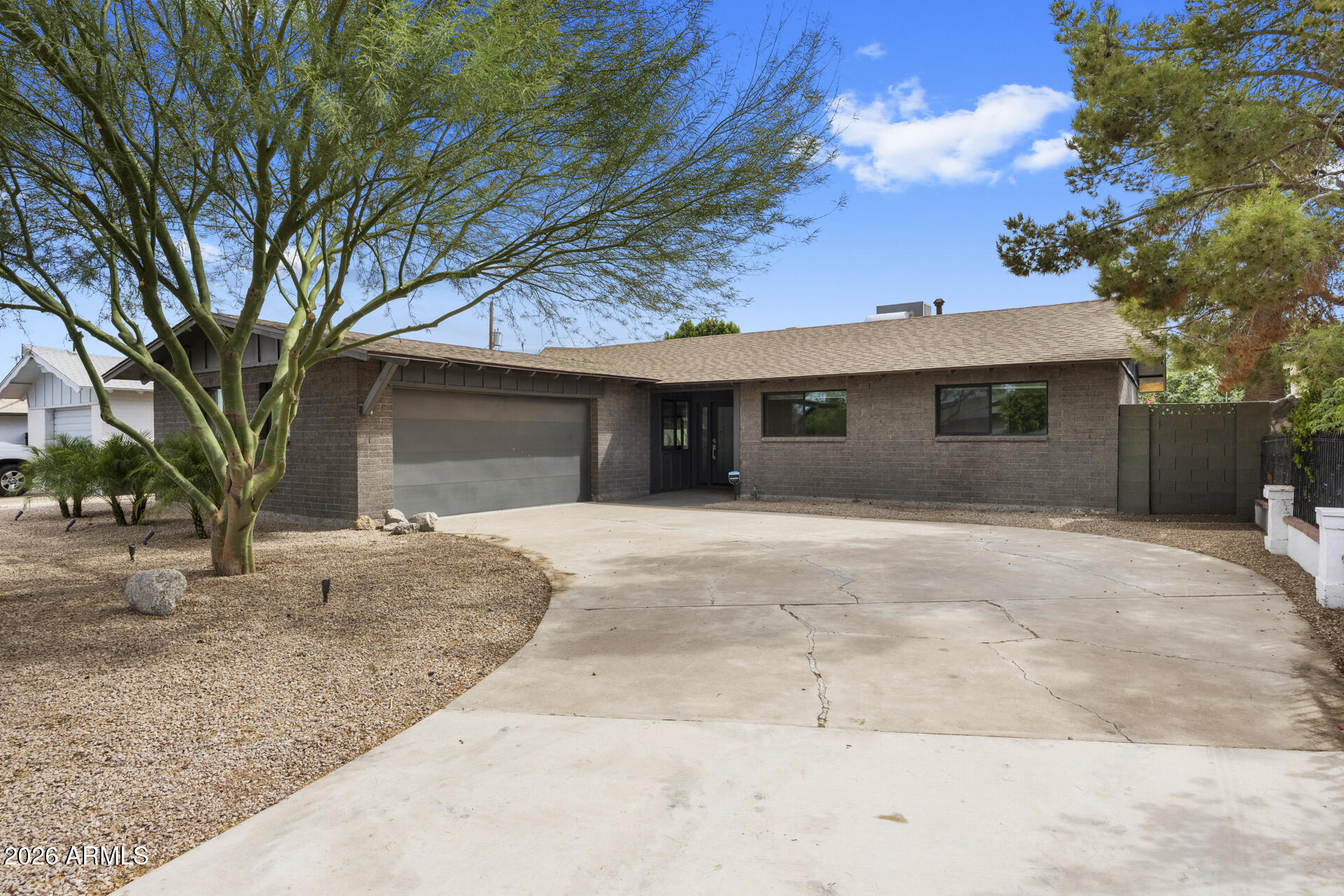 Single-story gray home with an attached garage, broad driveway, and gravel landscaping.
