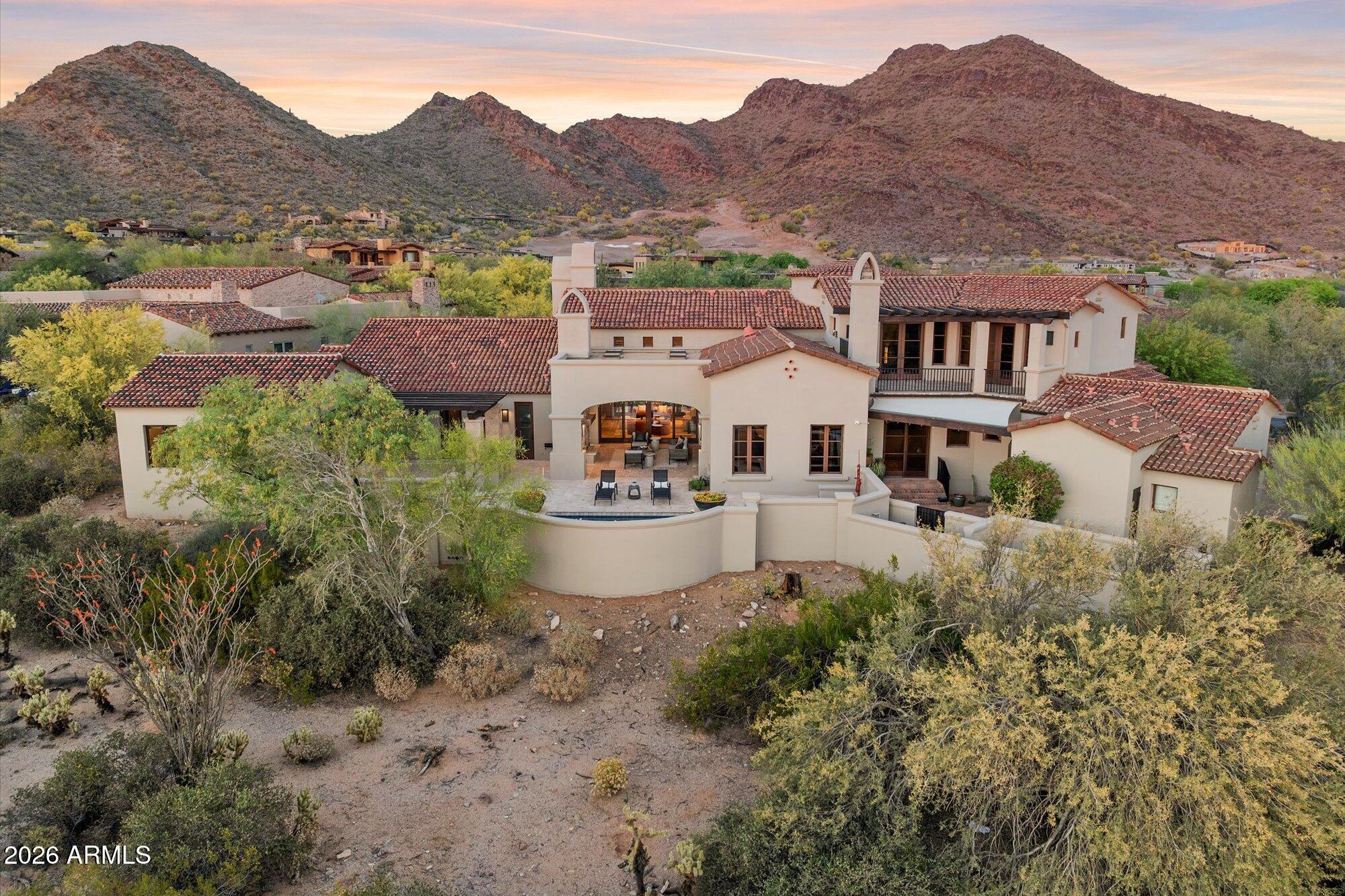 Aerial view of a tile-roofed desert home with a curved patio and mountain backdrop.