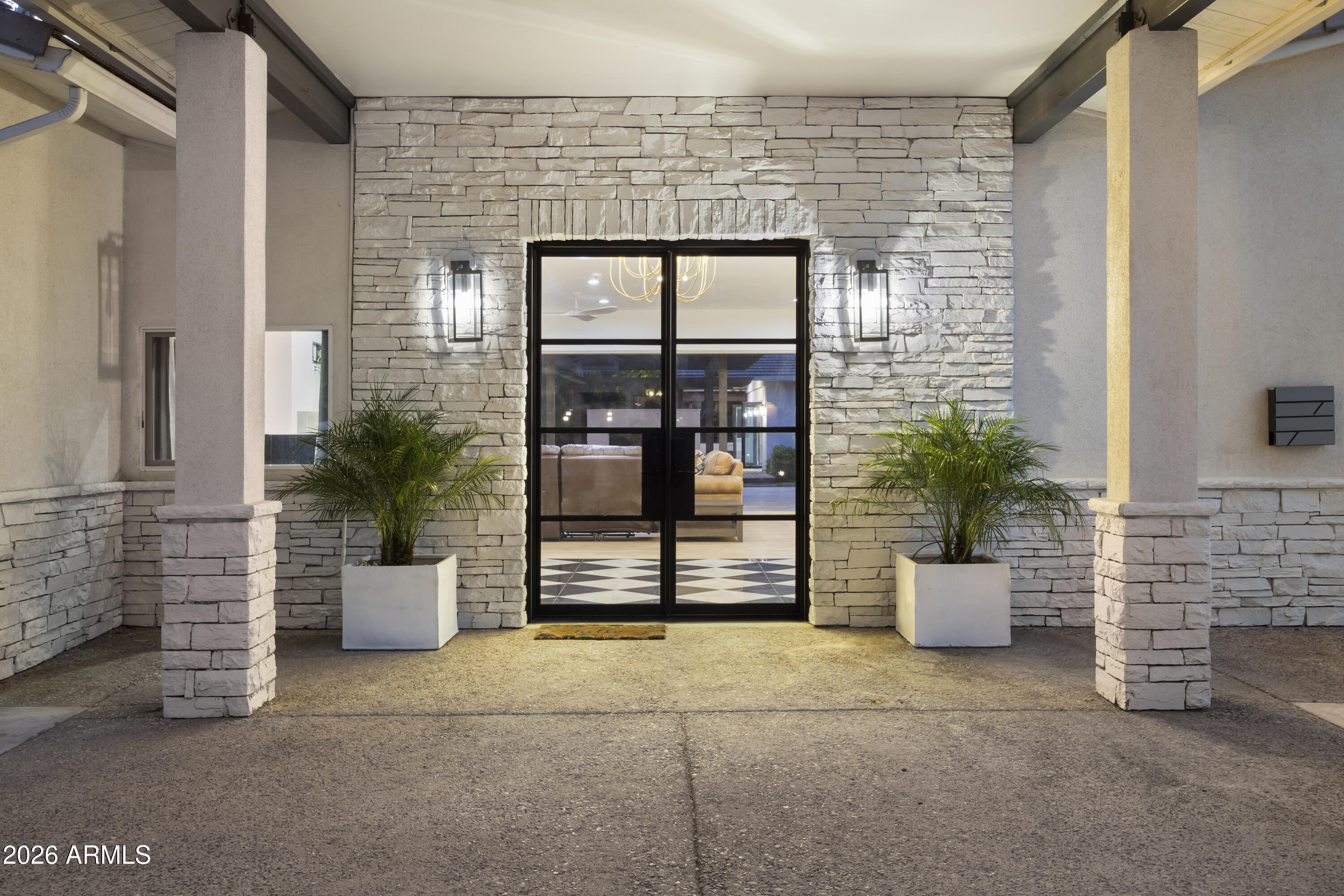 Home entrance with a stone facade, black-framed glass doors, and potted palms.