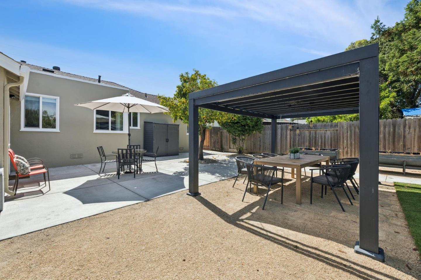 Backyard patio with a black pergola, outdoor dining table, and umbrella-shaded seating.