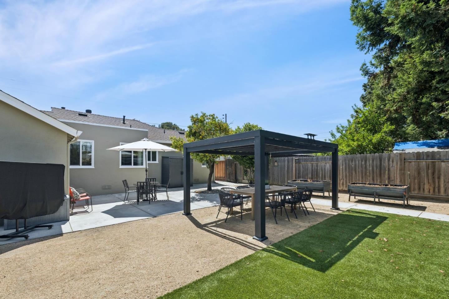 Backyard patio with a dark pergola, outdoor dining table, raised garden beds, and lawn.