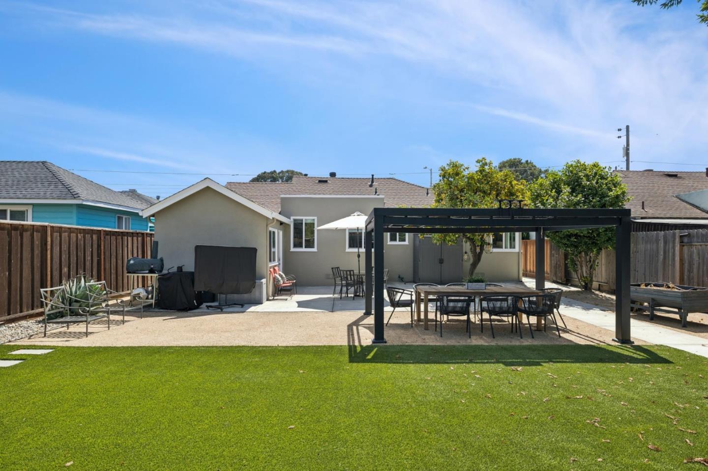 Backyard with a broad lawn, paved patio, and pergola-covered outdoor dining area.