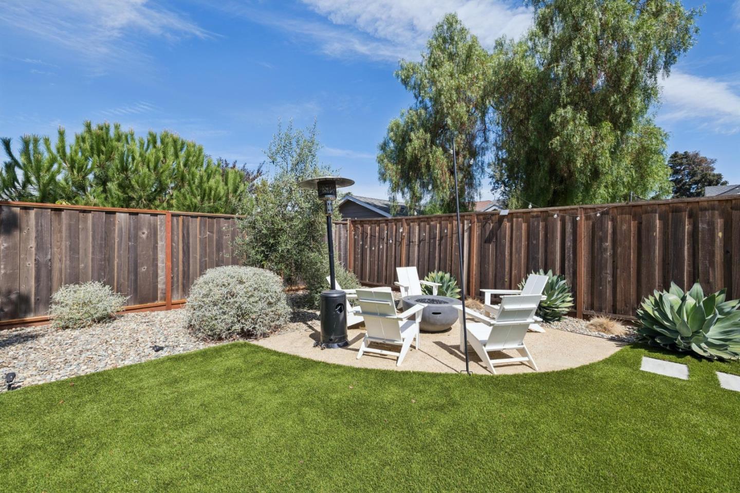 Fenced backyard with a green lawn and patio seating around a fire pit.