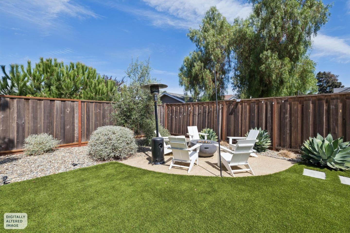 Backyard patio with white lounge chairs around a fire pit beside a green lawn.