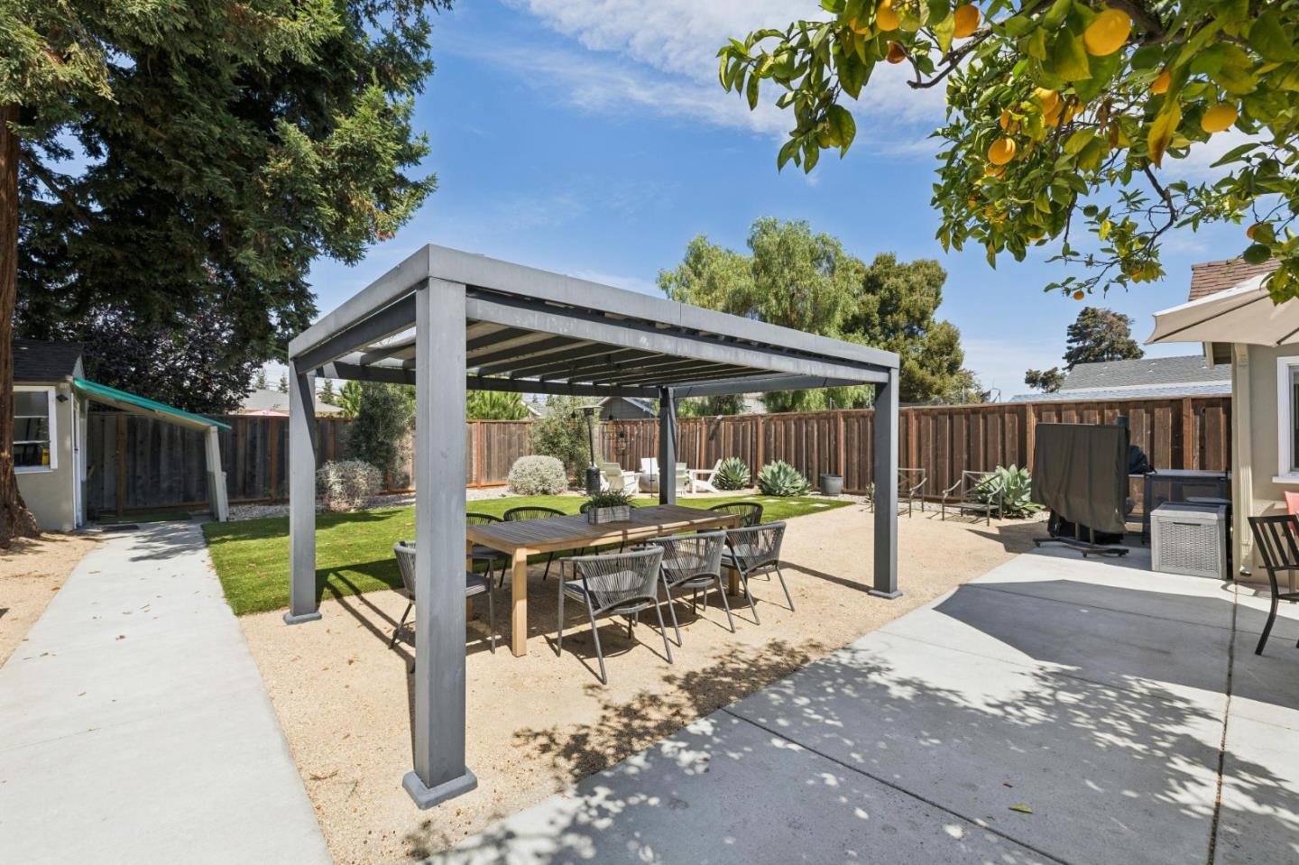 Backyard patio with a modern pergola shading an outdoor dining table beside a citrus tree.