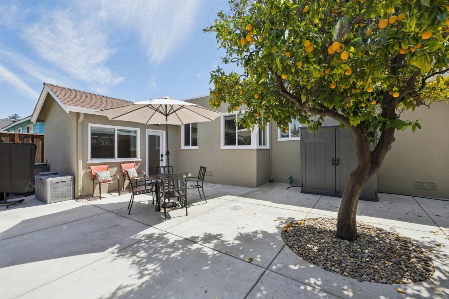 Backyard patio with outdoor dining set, large umbrella, and fruit-bearing citrus tree.