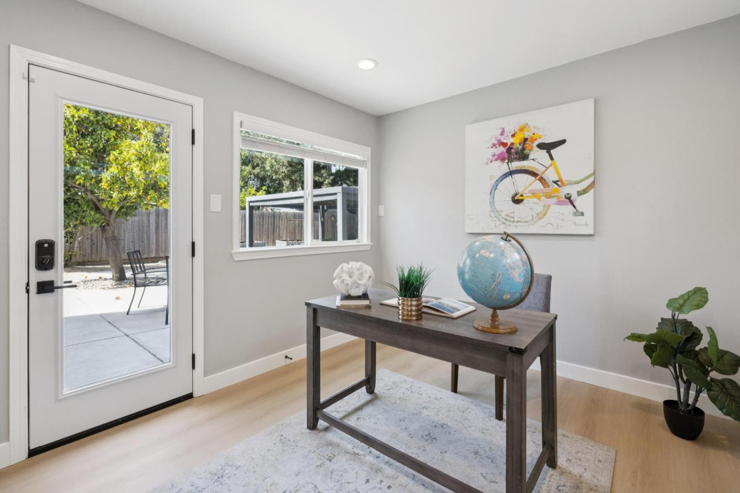 Furnished home office with a dark desk, globe, and glass door opening to a patio.