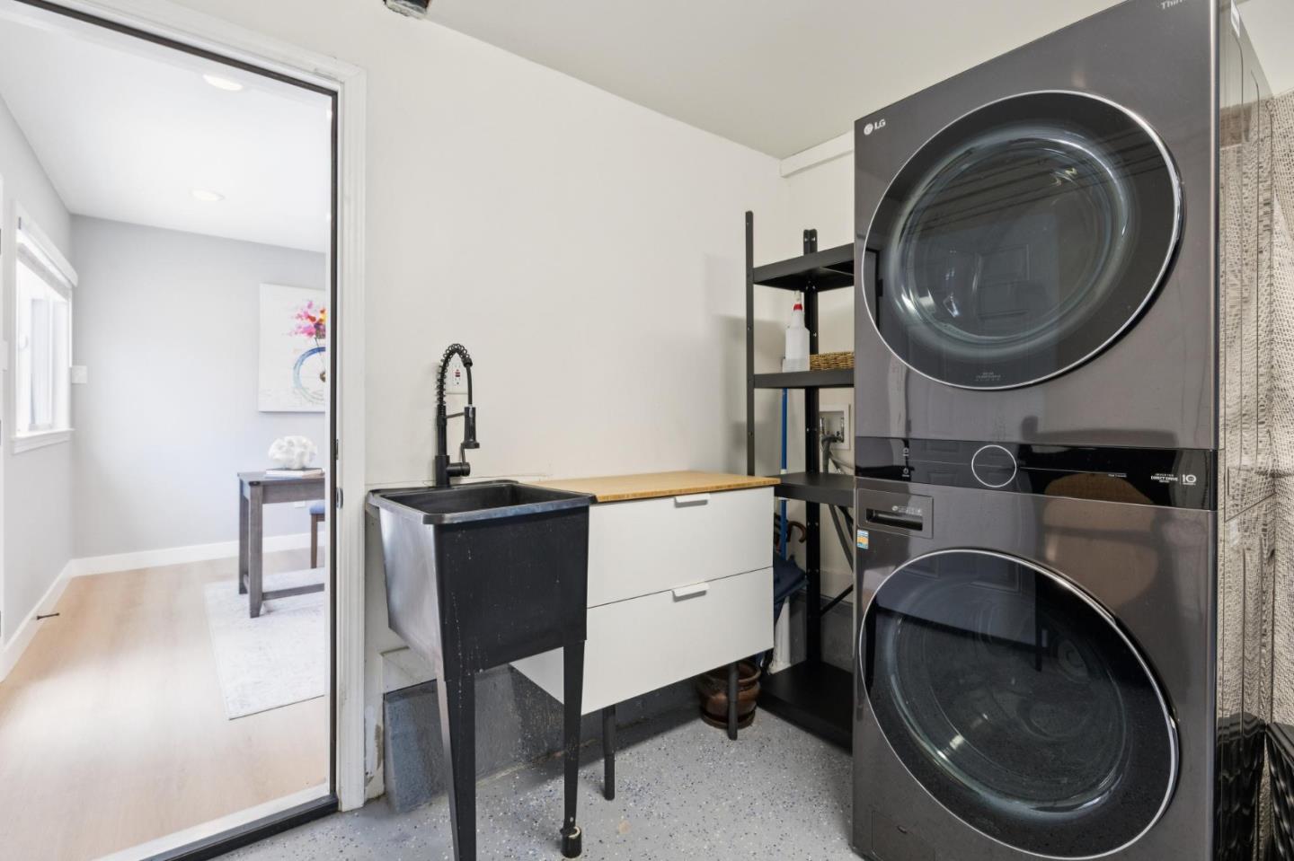 Laundry room with stacked washer and dryer beside a deep utility sink and wood countertop.