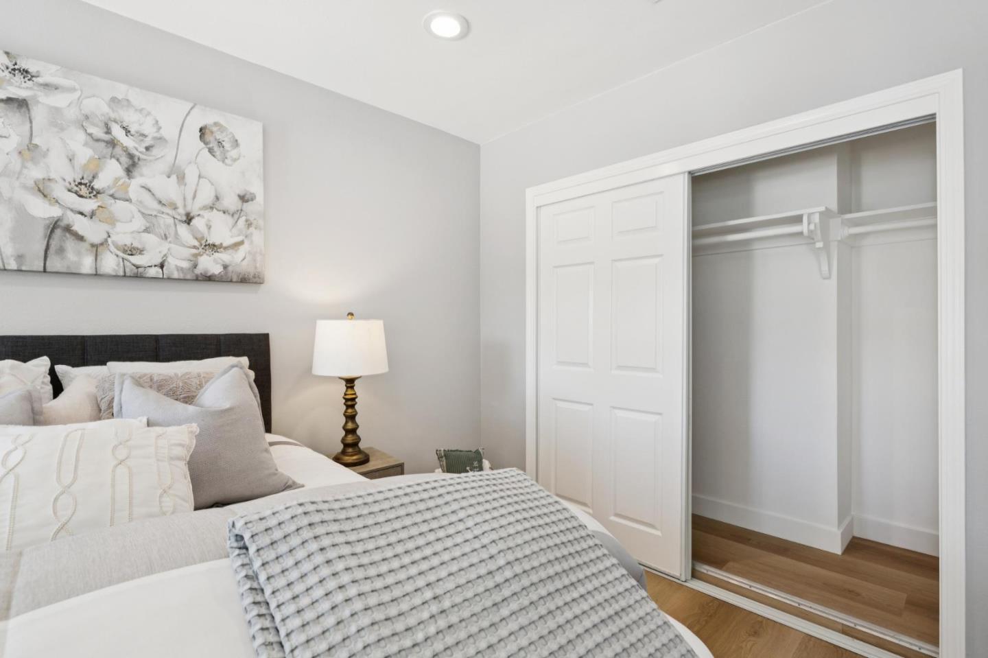 Staged bedroom with a neatly made bed, floral wall art, and an open sliding closet.