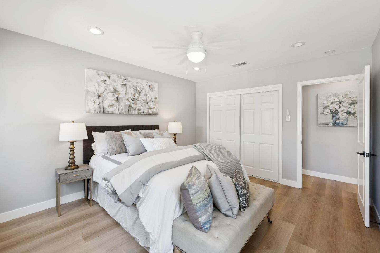 Staged bedroom with a white bed, dark headboard, floral wall art, and mirrored closet doors.