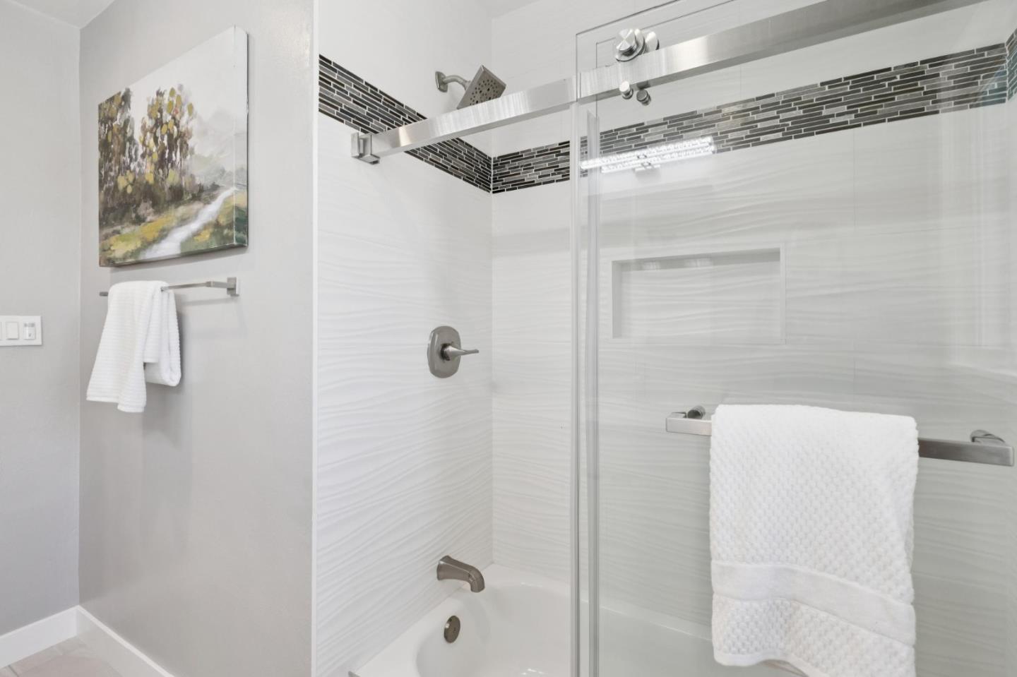 Bathroom with glass-enclosed tiled tub and shower, dark mosaic accent band, and white towels.