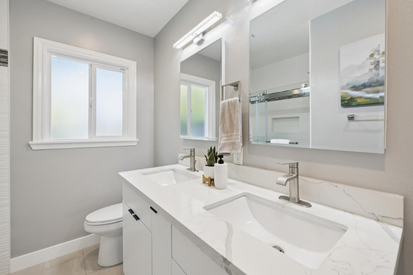 Bright bathroom with a white double vanity, veined countertops, and large mirrored cabinets.