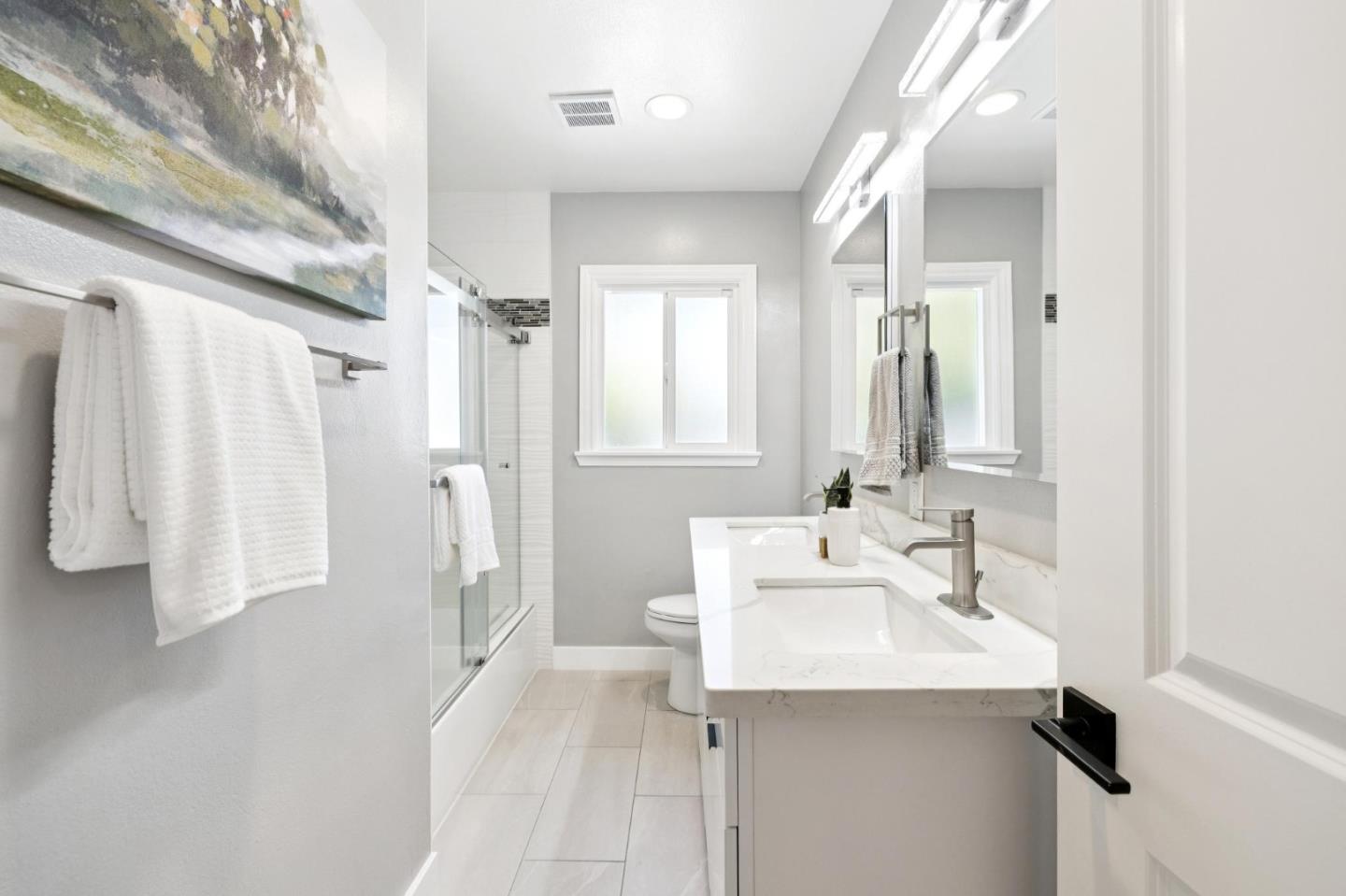 Bright bathroom with a long white vanity, large mirrors, and a glass-enclosed shower.