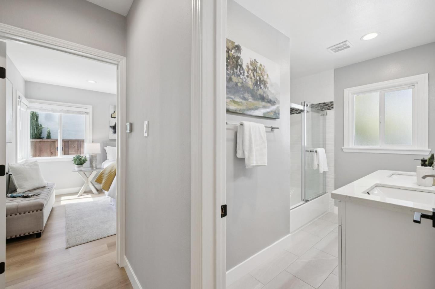 Bright bathroom with a glass-enclosed tub and white vanity, opening onto a bedroom.
