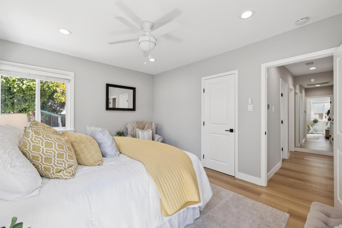 Staged bedroom with a yellow quilt, patterned pillows, and a window overlooking greenery.