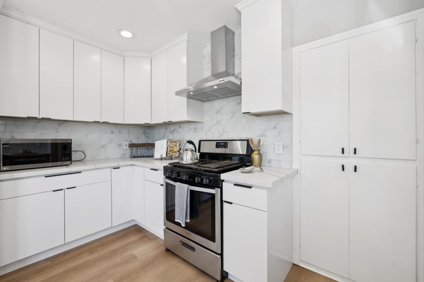 Modern white kitchen with marble-pattern backsplash, stainless steel range, and wood flooring.