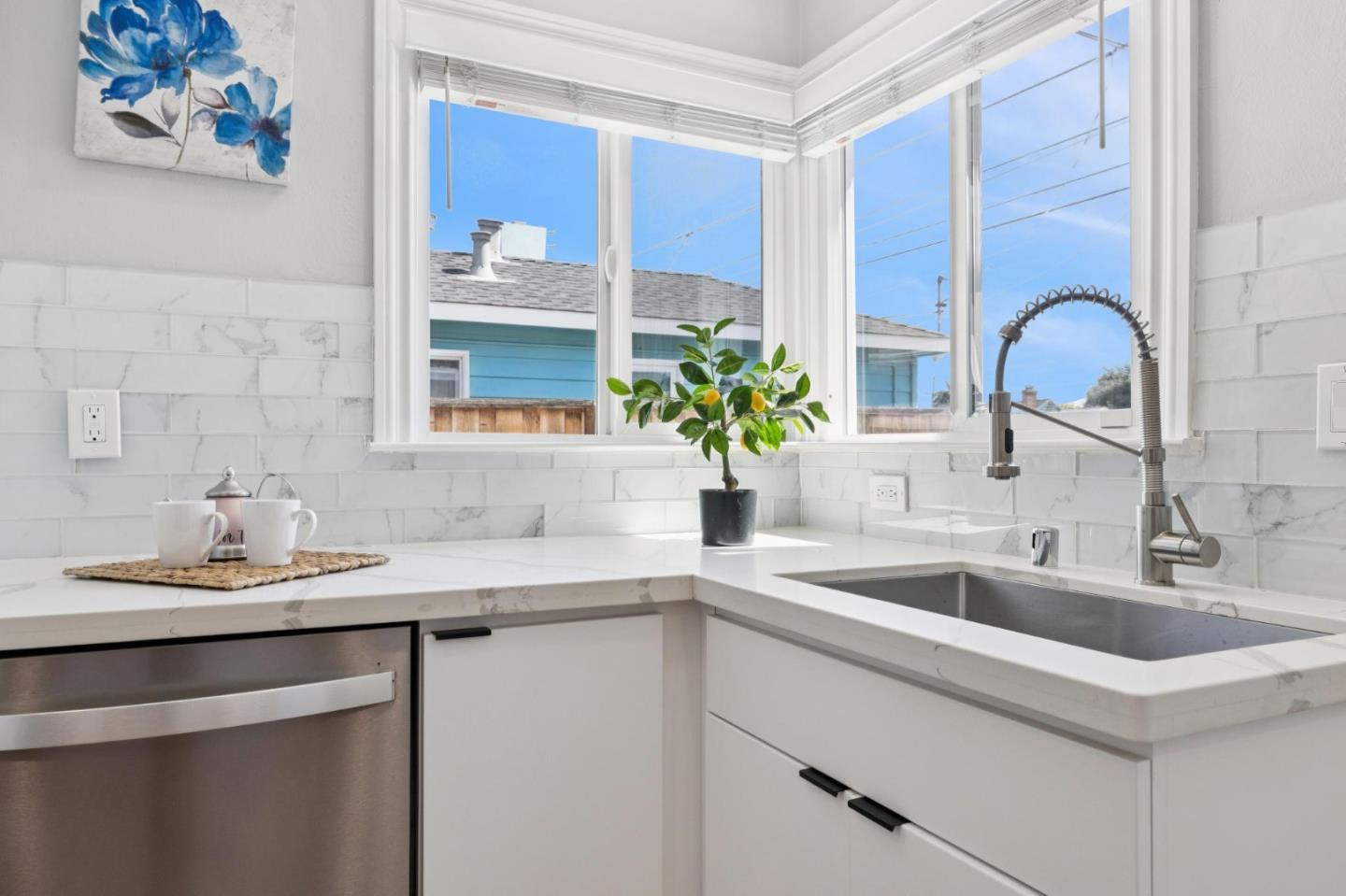 Kitchen with white marble counters, a deep sink beneath corner windows, and a potted citrus tree.