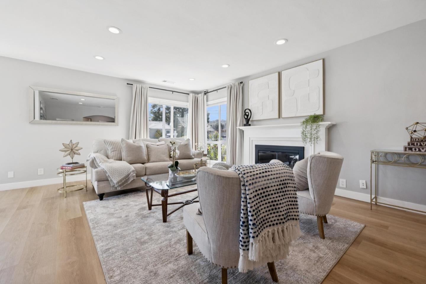 Staged living room with a white fireplace, large windows, and neutral furnishings.