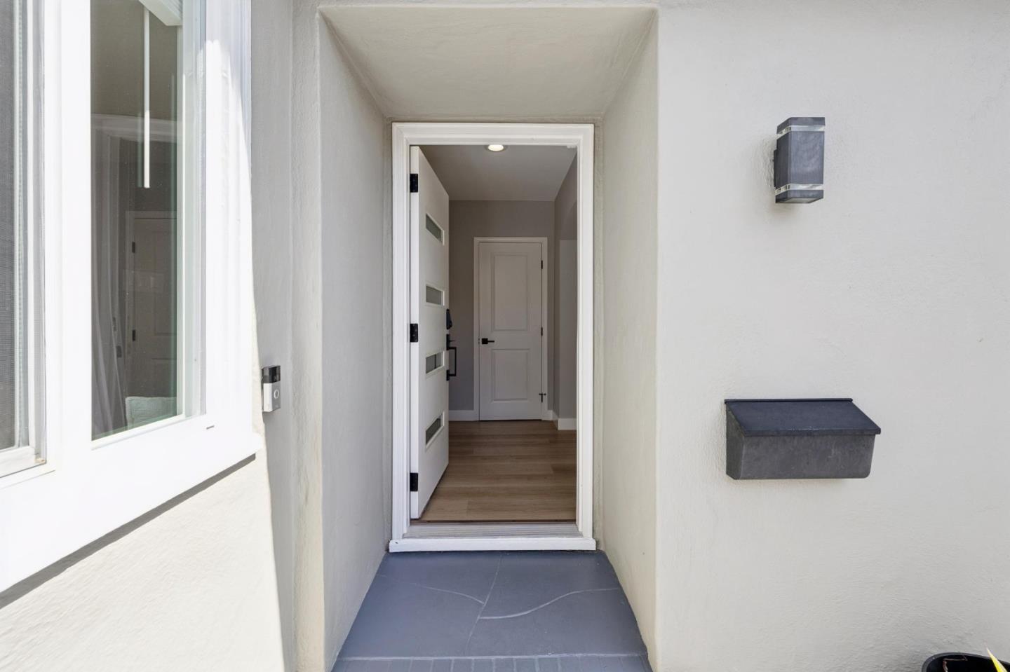 Recessed home entry with an open white door, gray tile porch, and wall-mounted mailbox.
