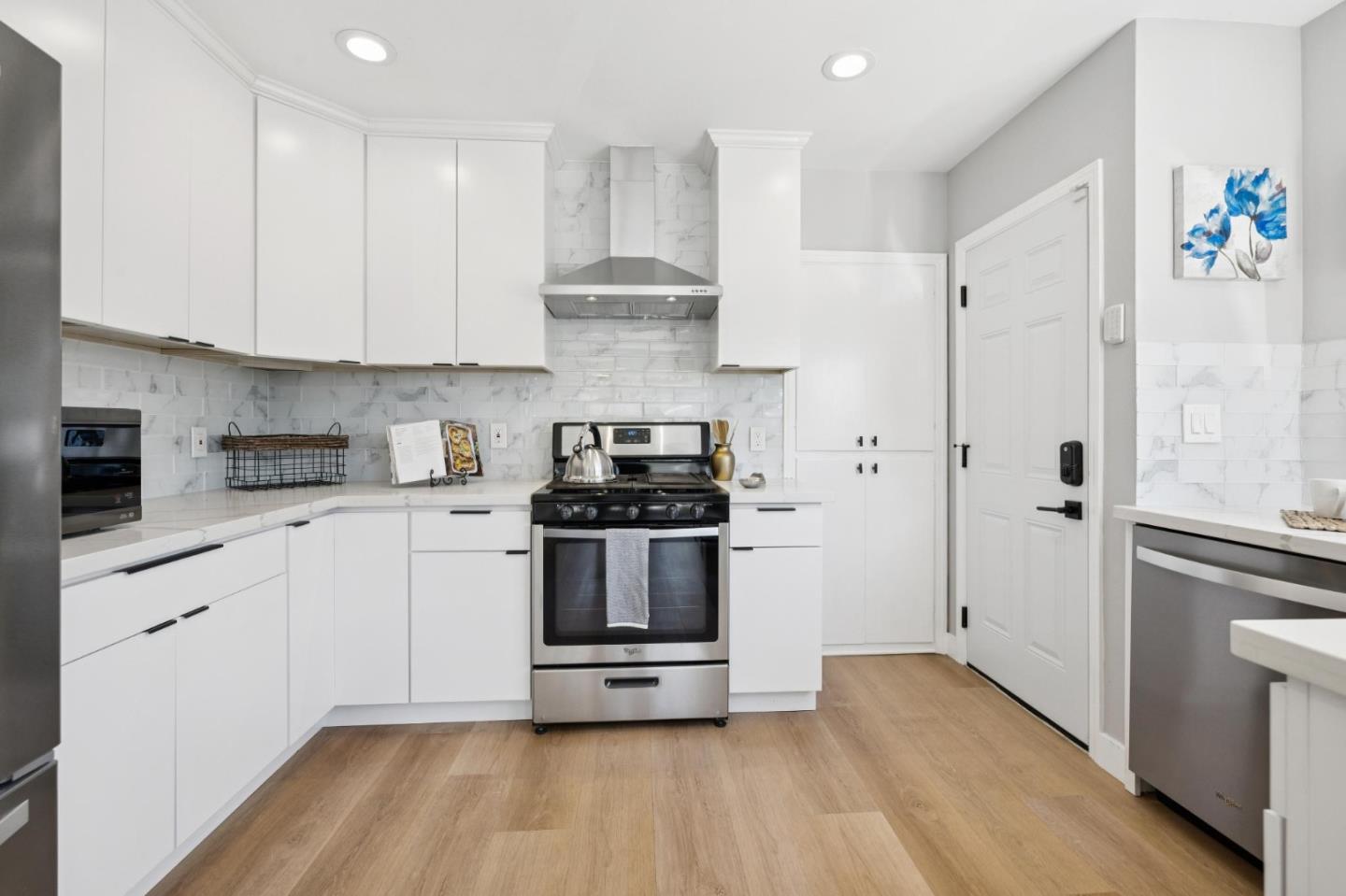 Updated kitchen with white cabinetry, marble-look backsplash, stainless steel range, and light wood floors.